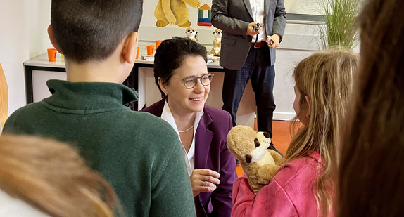 Ministerin Gentges überreicht einem Kind das Maskottchen