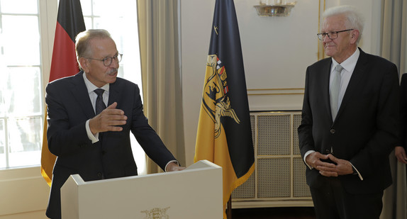 Franz Fehrenbach (links) und Ministerpräsident Winfried Kretschmann (rechts) stehen stehen im Runden Saal der Villa Reitzenstein vor Fahnen.