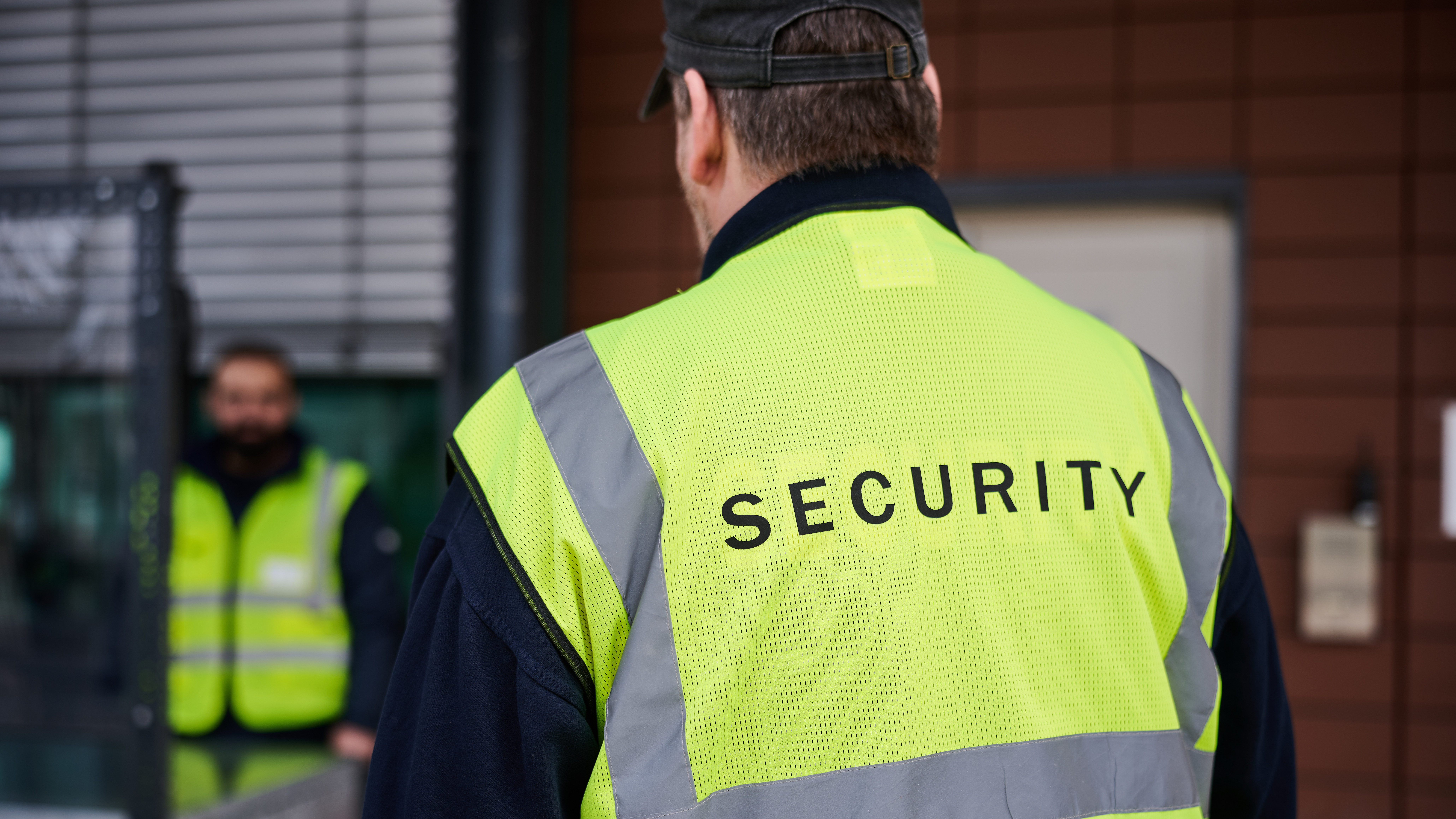Das Bild zeigt einen Mann vom Sicherheitsdienst, der eine gelbe Weste mit der Aufschrift "Security" trägt. 