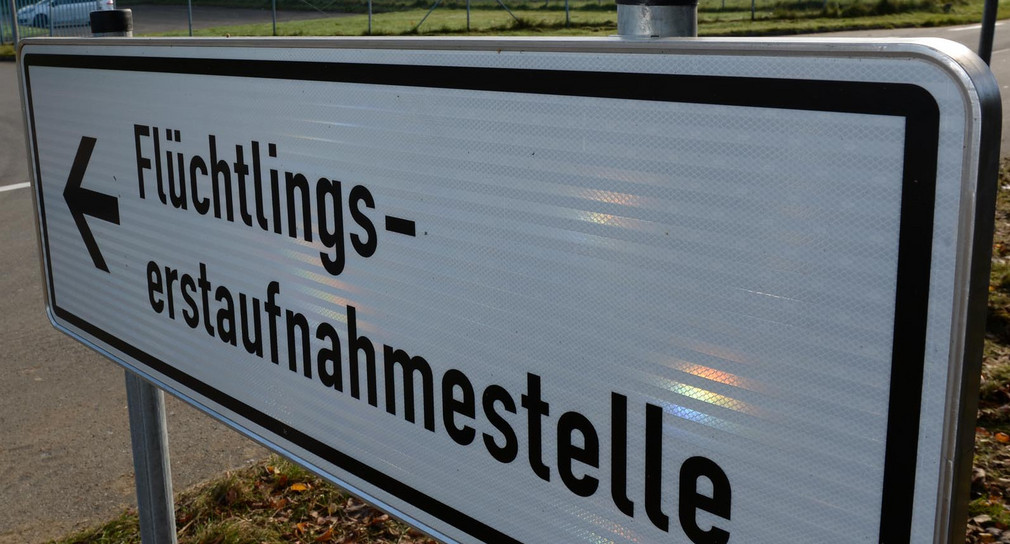 Ein Schild mit der Aufschrift „Flüchtlingserstaufnahmestelle“, im Hintergrund ein Fahrzeug an einer Einfahrt.