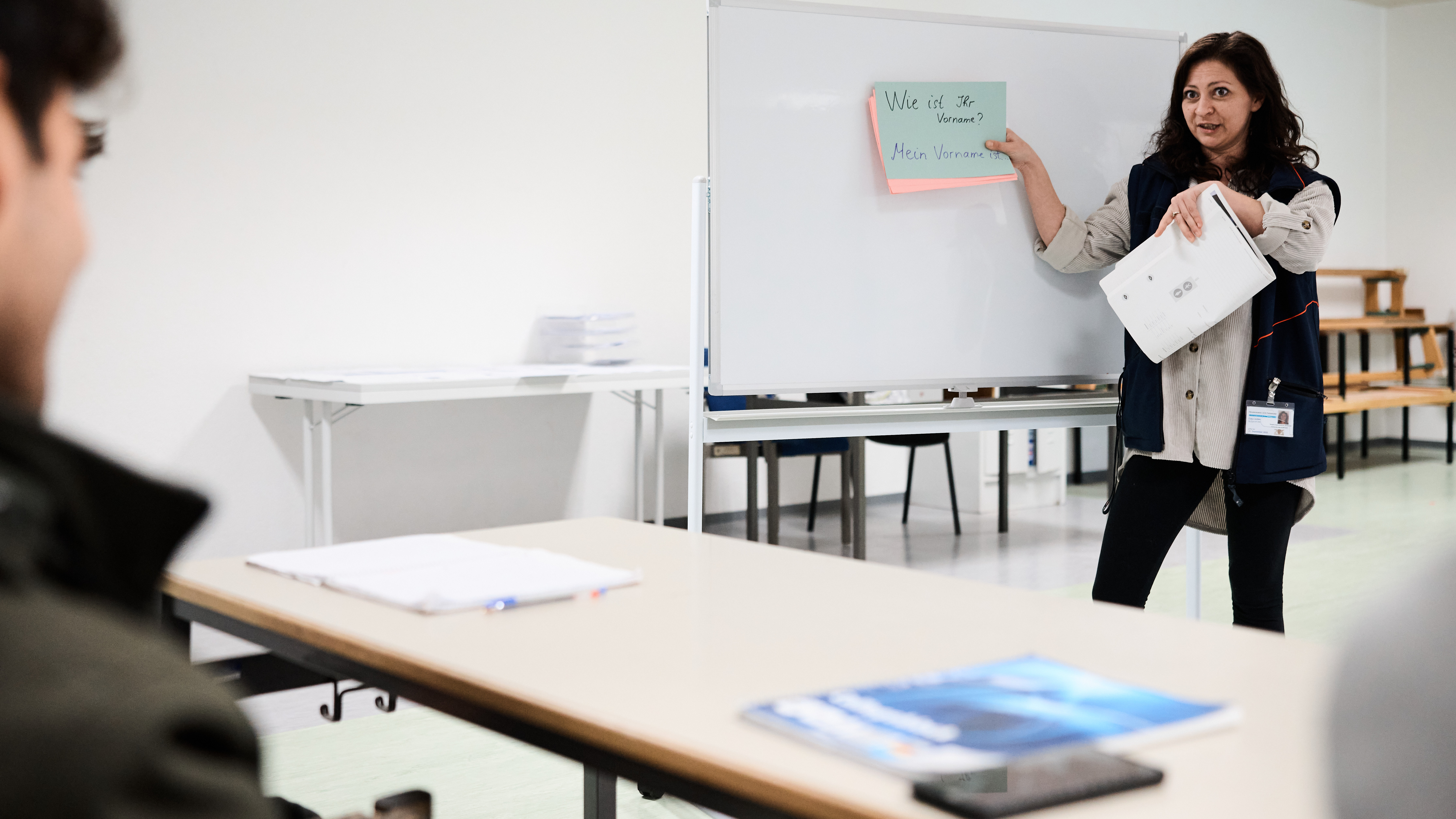 Das Bild zeigt eine Lehrerin beim Unterrichten eines Erwachsenen durch Schaubilder.