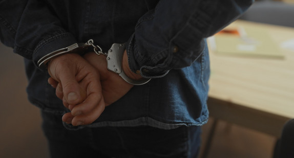 Close-up of a man handcuffed in a dimly lit indoor space, depicting an arrest scenario